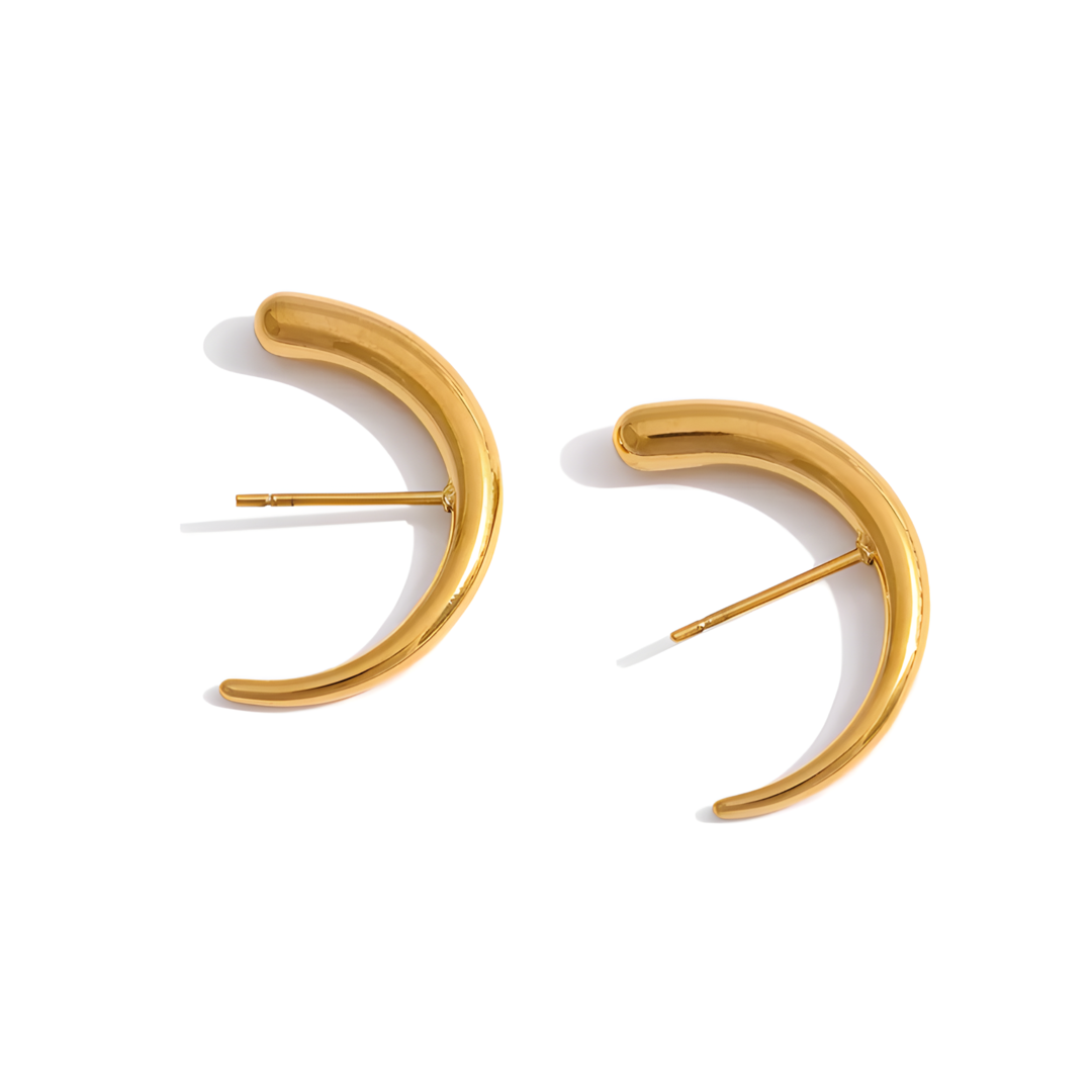 A pair of Moon Stud Earrings made of stainless steel, gently curving to nestle partly within the ear and beneath the earlobe. The earrings are 2.5cm in length and vary in thickness from 0.2cm to 0.4cm.